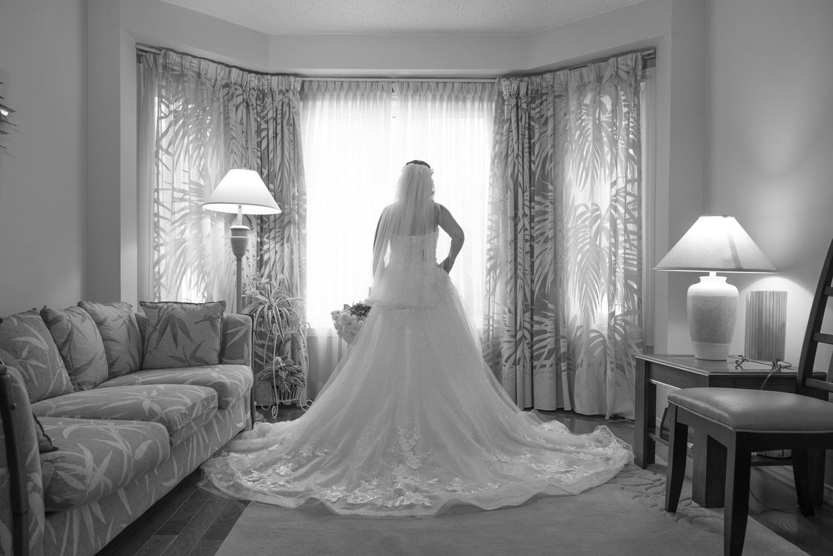 A bride looks out a bay window, illuminated by soft light, in an intimate moment before the wedding.