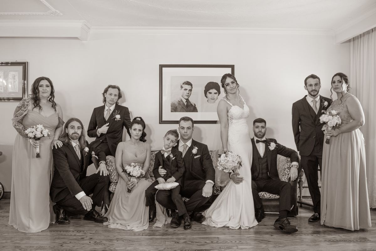 A formal sepia-toned wedding portrait of the bride and groom with their bridal party in an indoor setting.