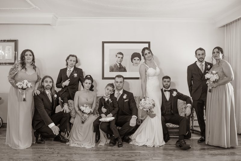 A formal sepia-toned wedding portrait of the bride and groom with their bridal party in an indoor setting.