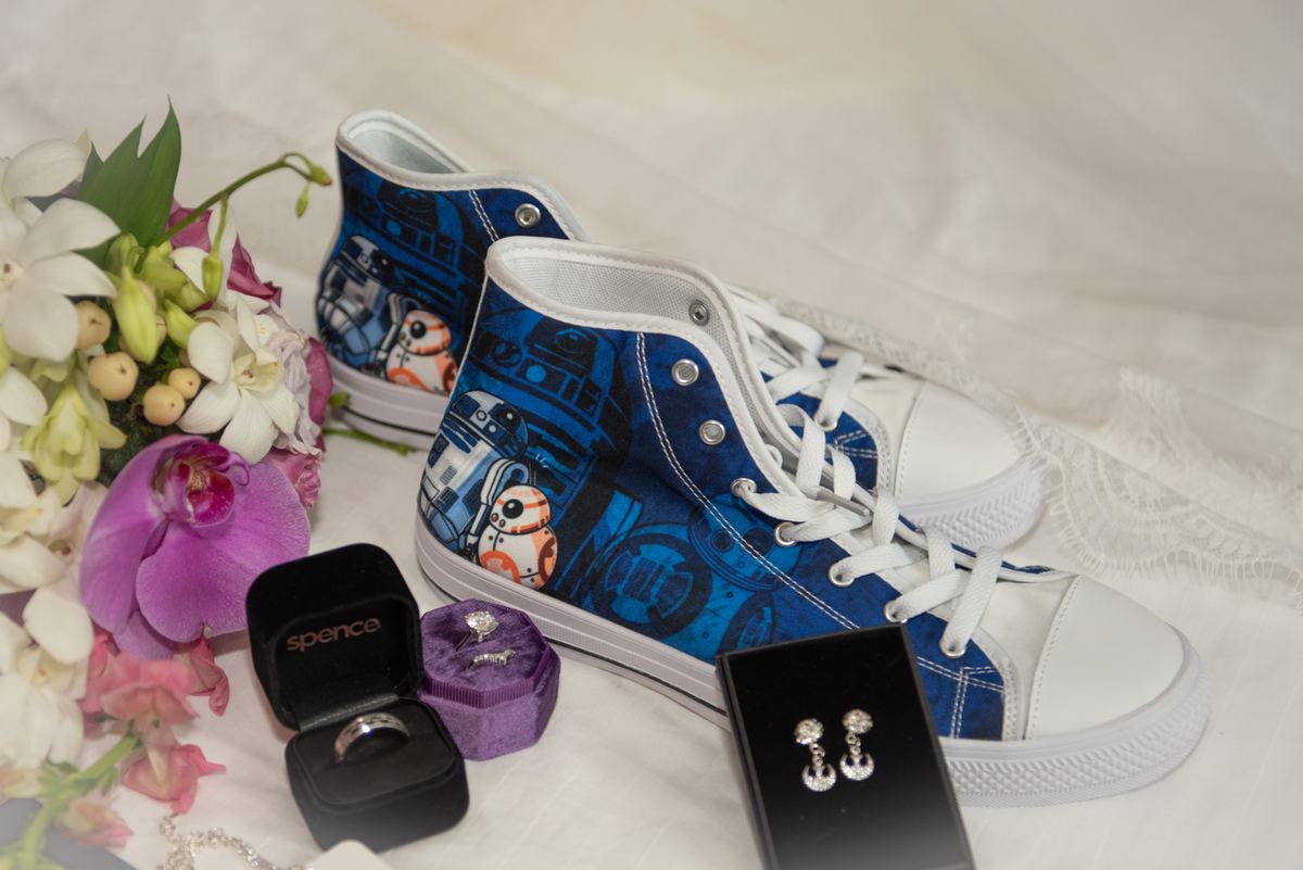A bride's preparation with Star Wars sneakers beside wedding rings and flowers, set against a white backdrop.
