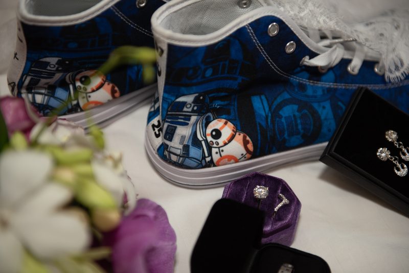 Blue Star Wars sneakers with R2-D2 and BB-8 next to a velvet ring box and earrings case, under soft light.