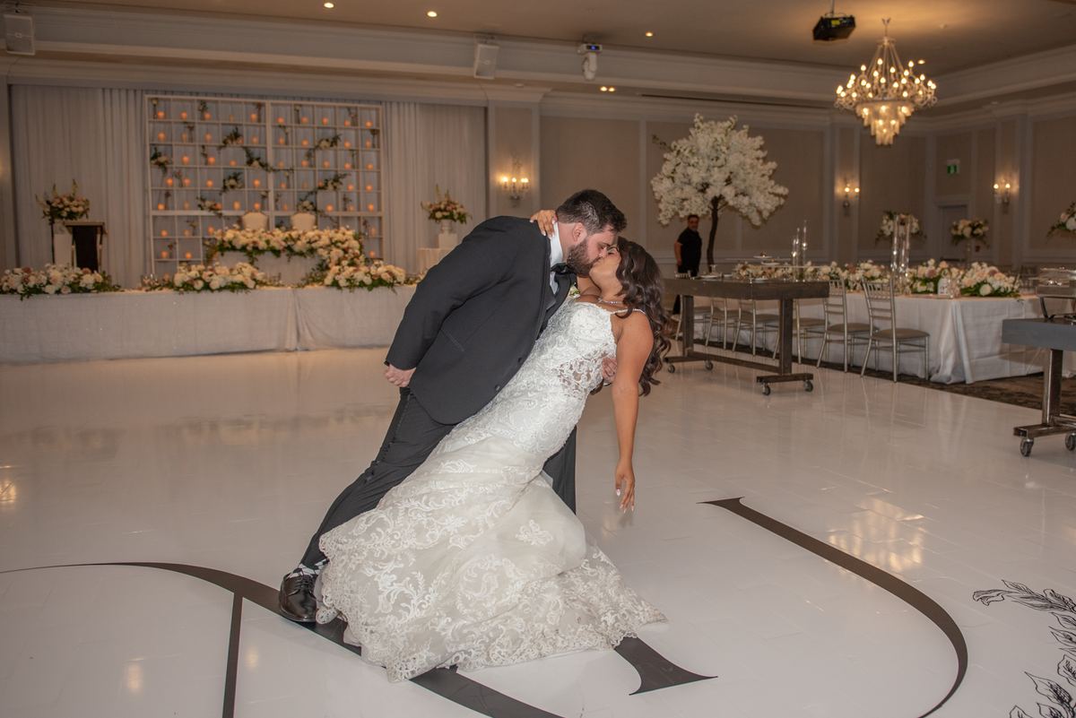 A bride and groom kiss on a decorated dance floor surrounded by flowers and candles, capturing the joy of their celebration.