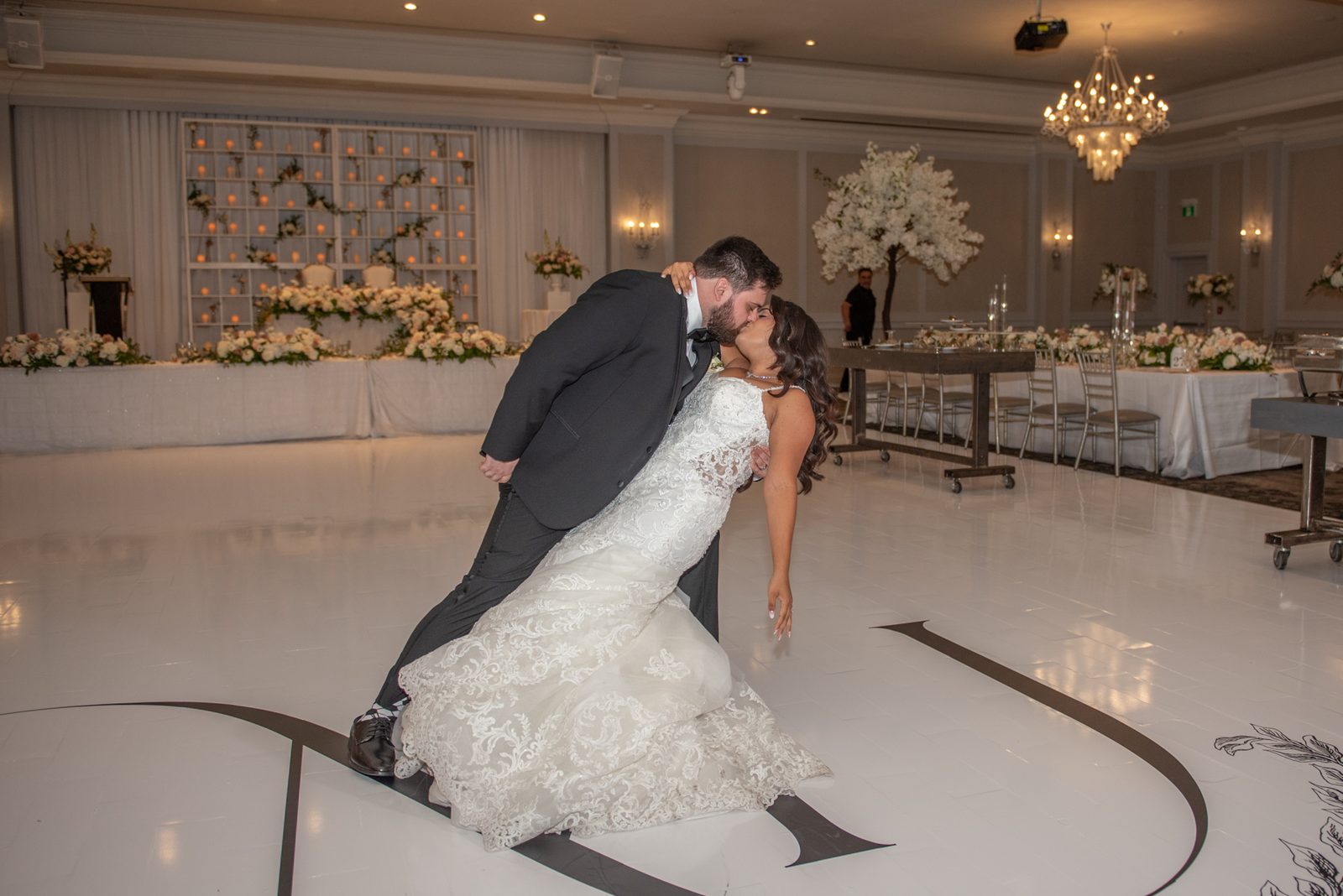 A bride and groom kiss on a decorated dance floor surrounded by flowers and candles, capturing the joy of their celebration.
