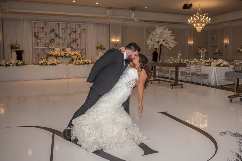 A bride and groom kiss on a decorated dance floor surrounded by flowers and candles, capturing the joy of their celebration.