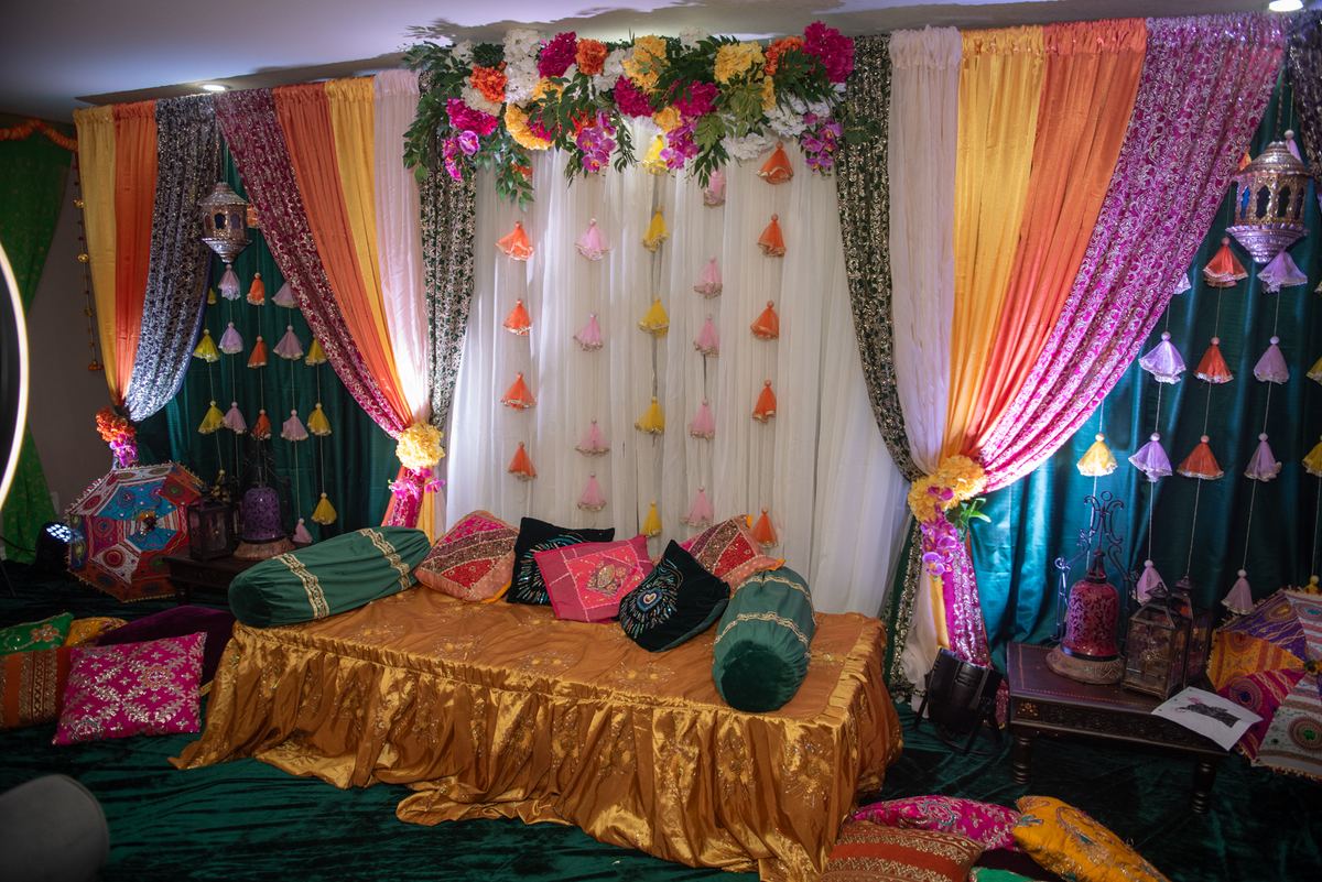 Richly colored drapes and hanging lanterns decorate an ornate ceremonial space with golden cushions.