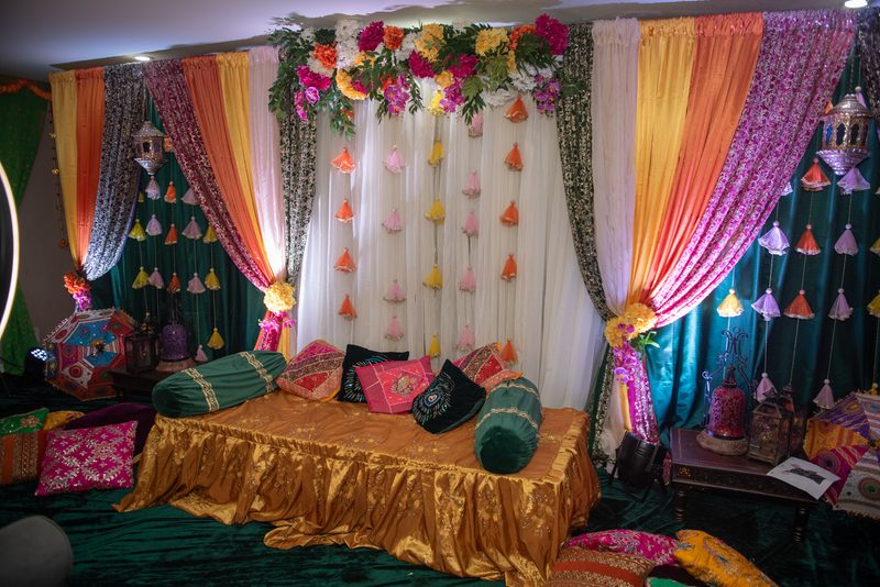 Richly colored drapes and hanging lanterns decorate an ornate ceremonial space with golden cushions.