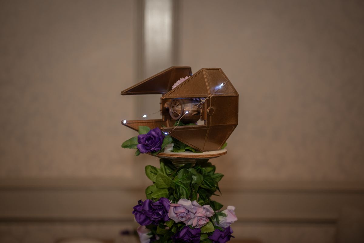 A detailed model of a Star Wars starship sits on a pedestal decorated with pastel flowers and greenery.