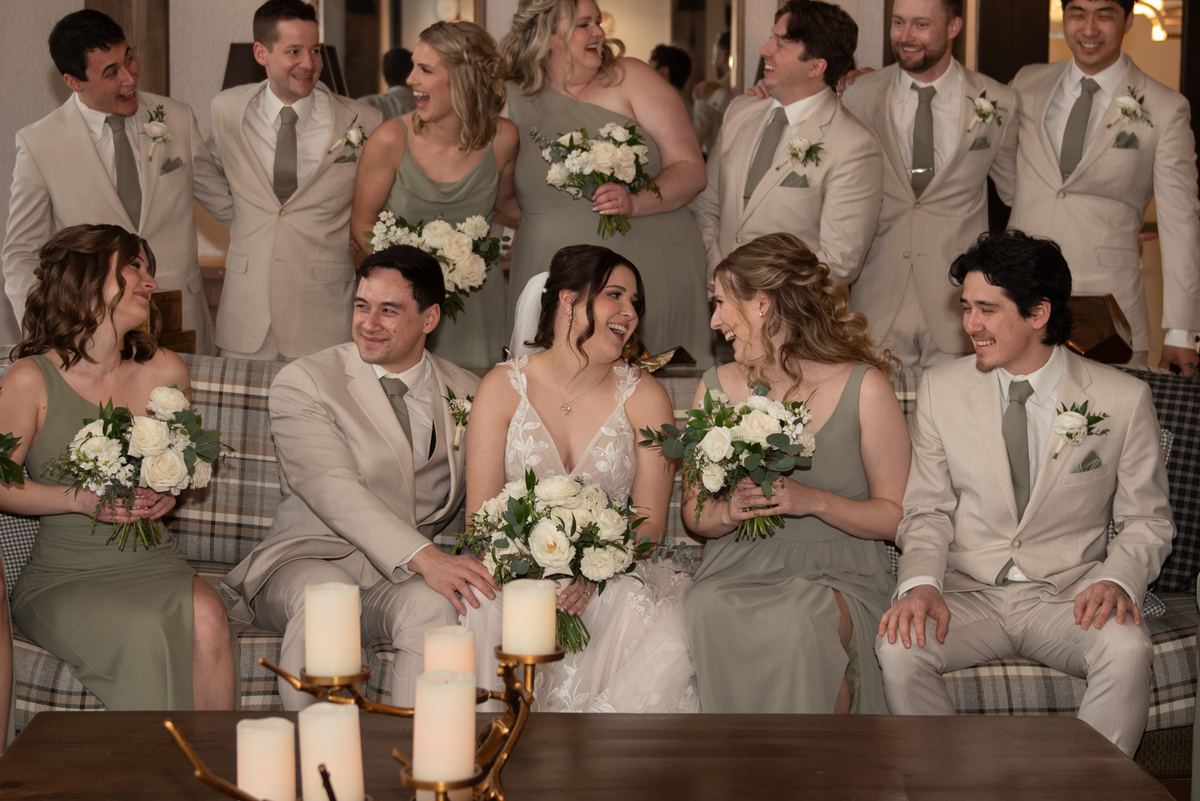 A joyful wedding party, including the bride and groom, gathers around a candlelit table, exuding warmth and camaraderie.