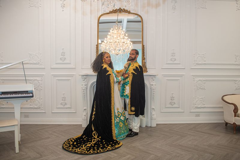 Salem and Shannon stand close in ornate black and gold robes, Salem smiling warmly as she touches Shannon's arm.