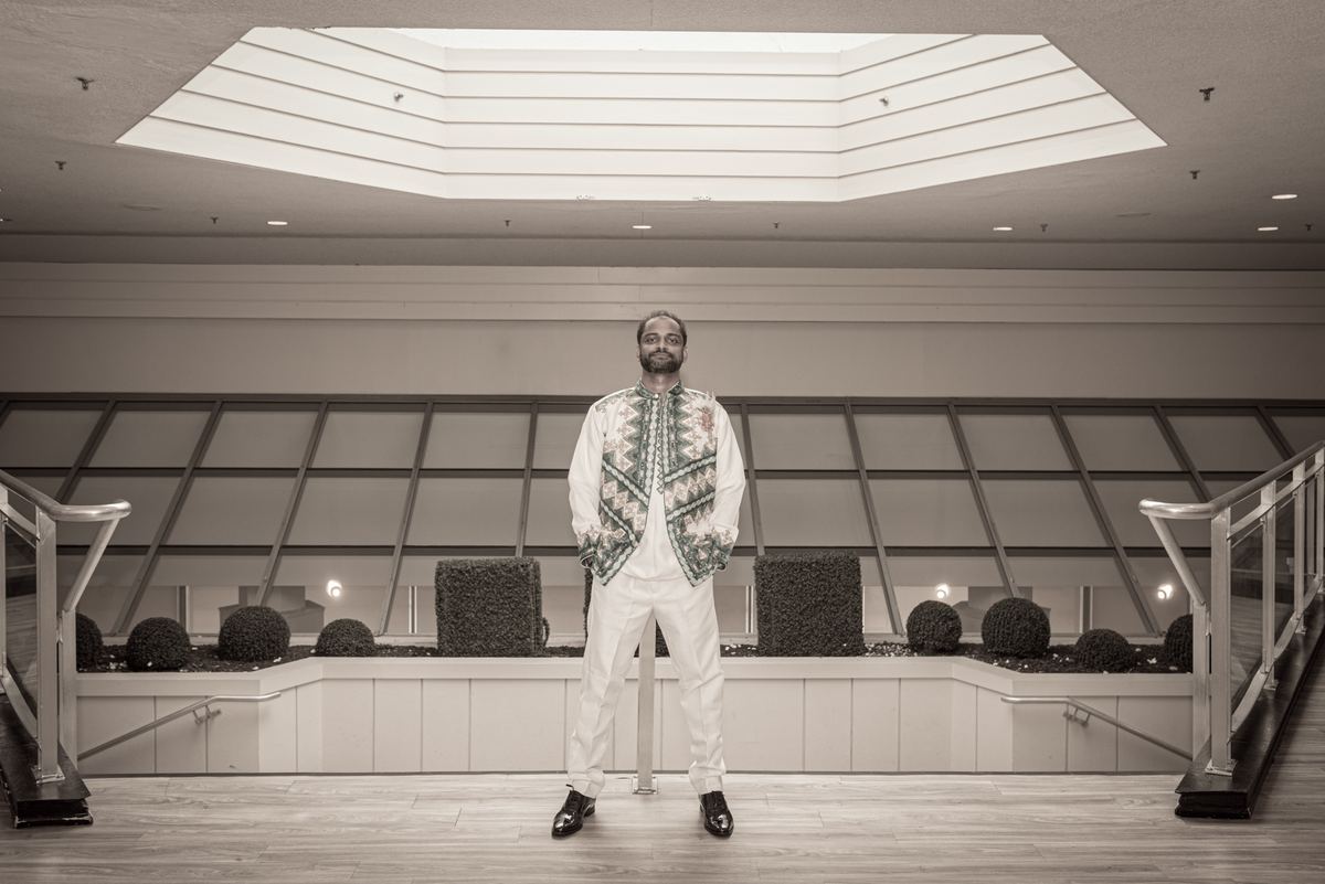 A man in white and a patterned vest stands in a modern atrium with geometric skylights and railings.