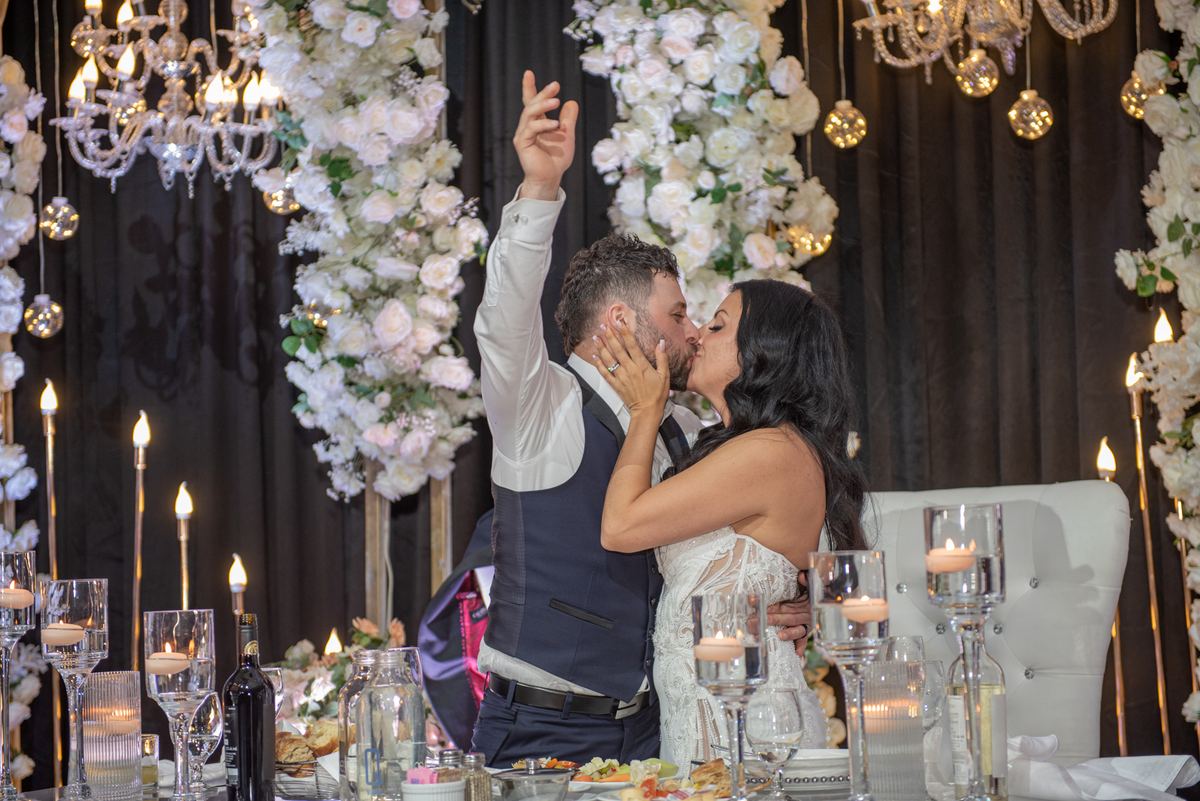 Sarah and Alessandro share an intimate kiss at their reception, surrounded by candlelight and hanging floral arches.