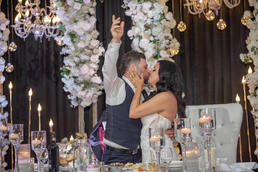 Sarah and Alessandro share an intimate kiss at their reception, surrounded by candlelight and hanging floral arches.