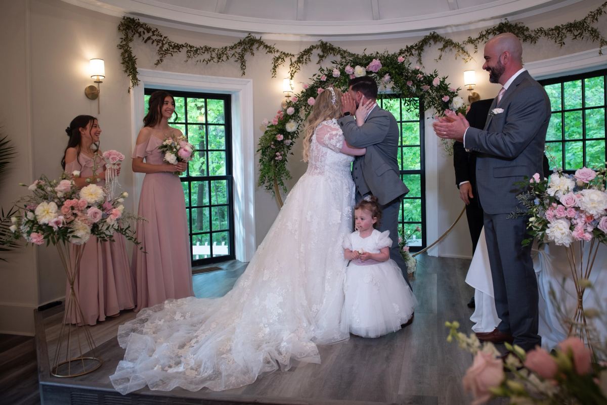 Josianne and Duarte share a passionate kiss at the altar, surrounded by floral arrangements and greenery.