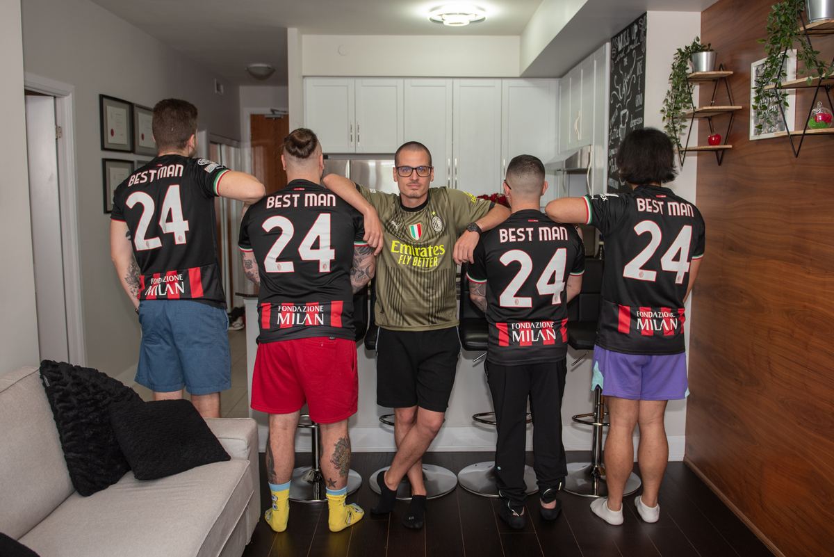 Four people in black 'BEST MAN 24' jerseys and one in a green 'Emirates Fly Better' jersey stand close in a modern kitchen.