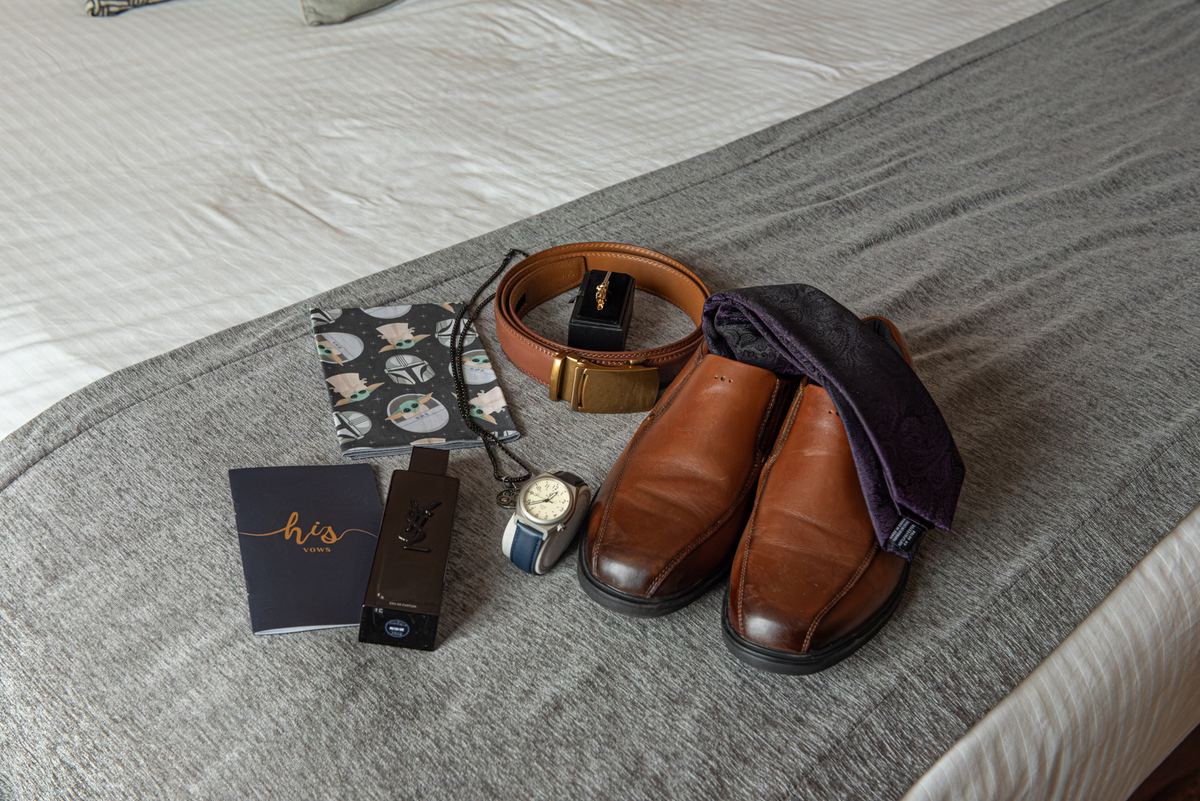 Men's formal items including loafers, belt, watch, fragrance, vows booklet, and Star Wars wallet on a bed.