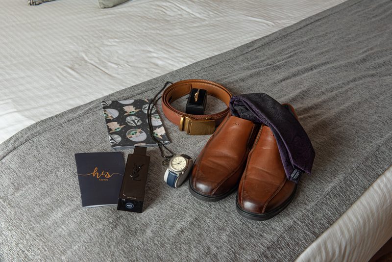 Men's formal items including loafers, belt, watch, fragrance, vows booklet, and Star Wars wallet on a bed.