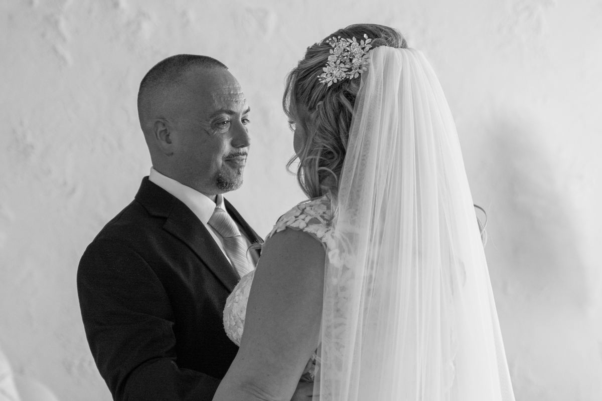A bride and her father share an emotional moment during a wedding, their faces illuminated by soft lighting.