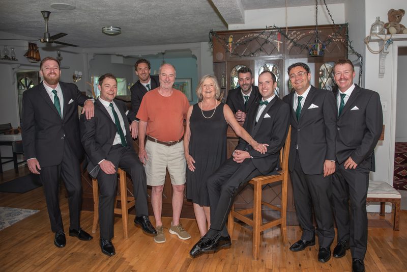 A group of people in dark suits and green ties, with one woman in a black dress and another man in an orange shirt.