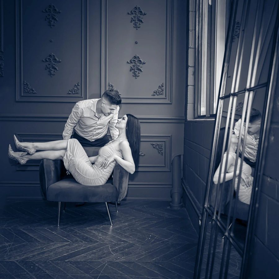 A couple photographed in a panelled studio in deep blue light, one carried in the other's arms.