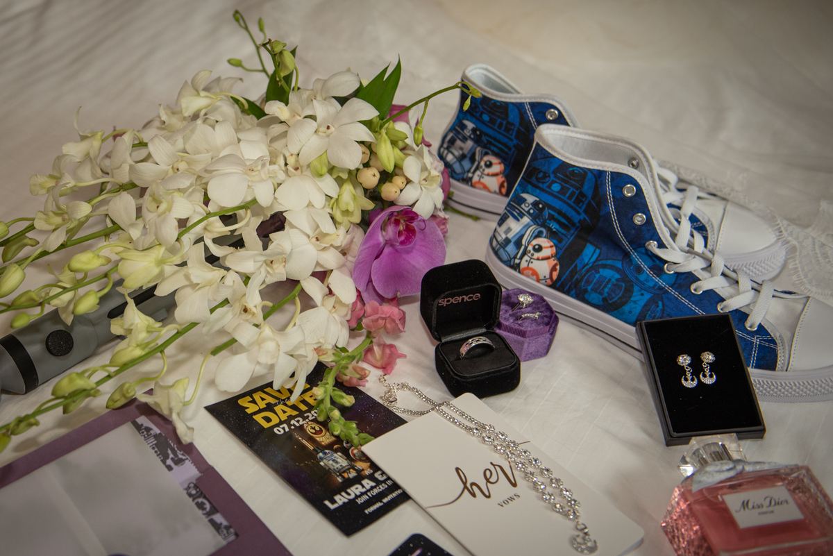 White orchids and pink flowers surround Star Wars sneakers, ring box, earrings, Save the Date card, perfume bottle.