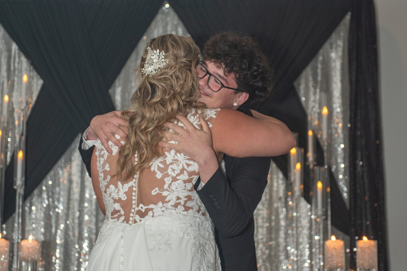 Candace and Felice share an intimate embrace at their wedding, surrounded by shimmering silver drapery and soft candlelight.