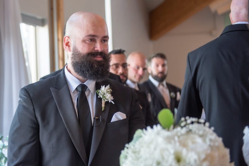 Tiago, dressed in a dark suit and white boutonnière, stands at the altar looking towards Kara's entrance.