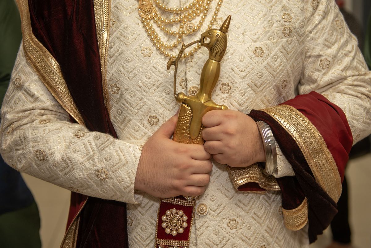 A person in traditional South Asian attire holds a ceremonial golden sword, emphasizing the moment's honor and presentation.