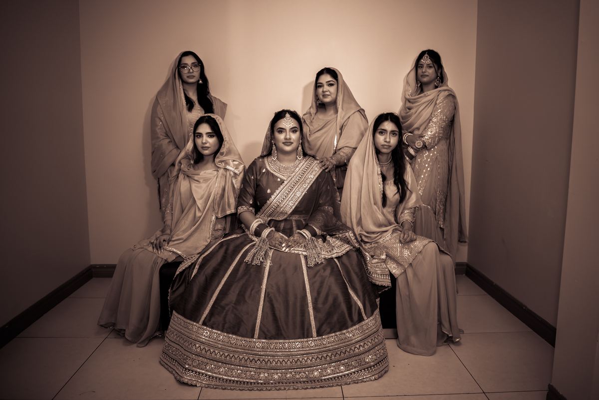 A bride and her female relatives pose in traditional attire in a narrow corridor, creating an intimate pre-ceremony scene.