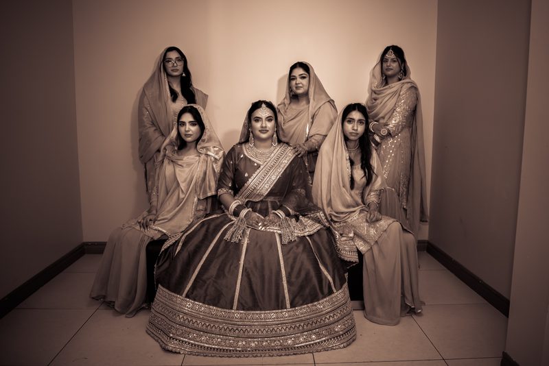 A bride and her female relatives pose in traditional attire in a narrow corridor, creating an intimate pre-ceremony scene.