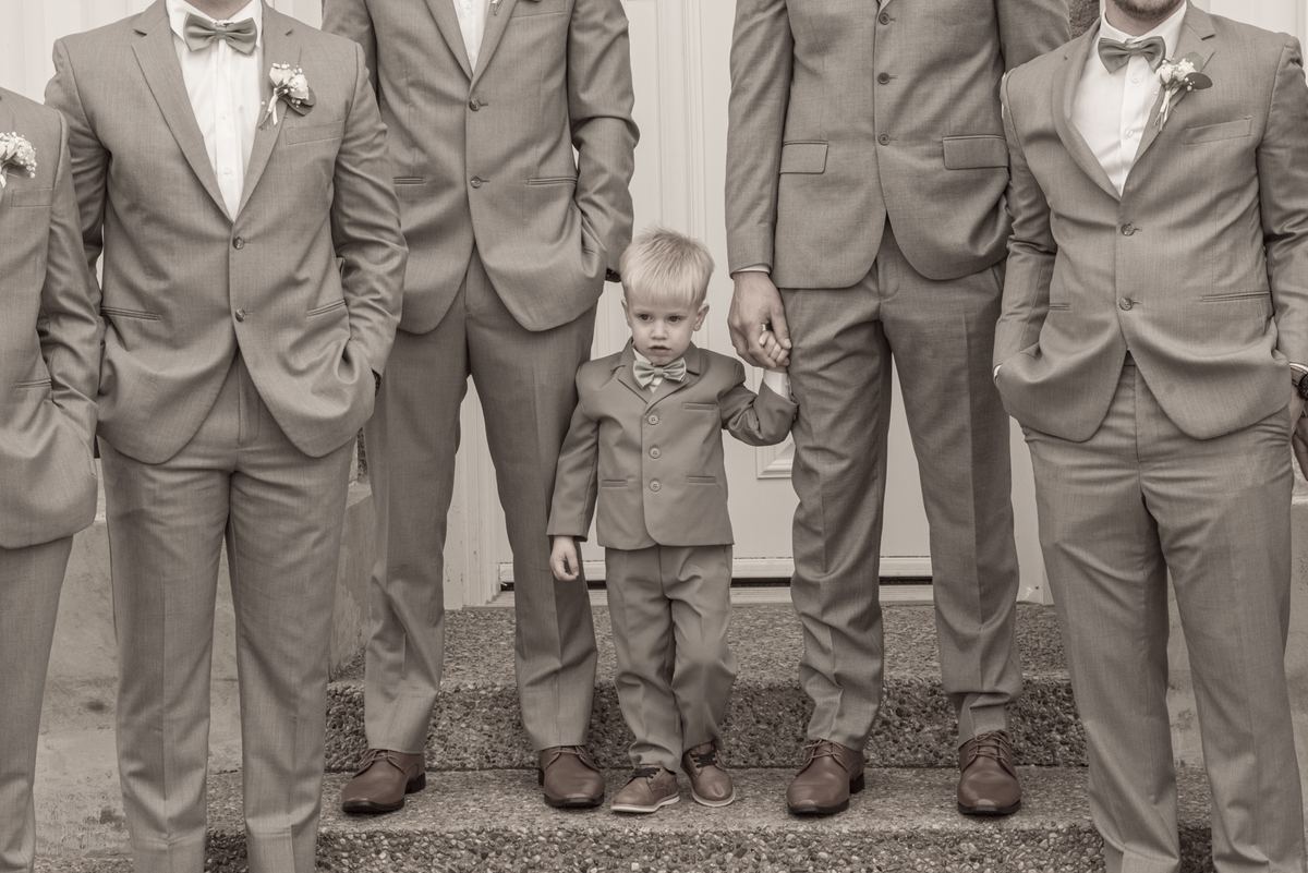 A young boy in a tuxedo stands with adult family members and other children dressed formally on stone steps.