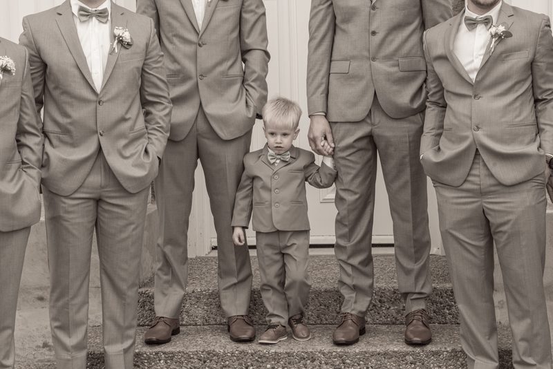 A young boy in a tuxedo stands with adult family members and other children dressed formally on stone steps.