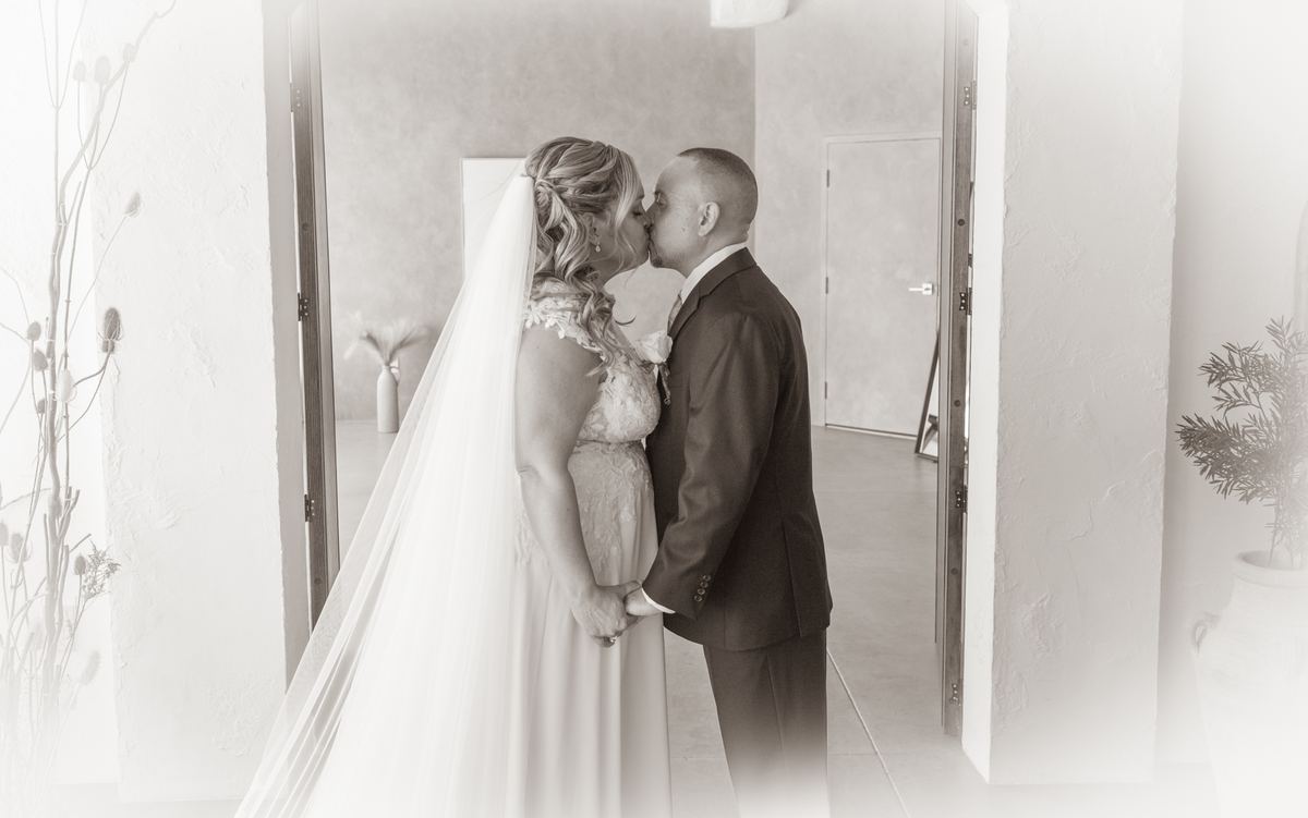 A bride and groom exchange a loving kiss in a minimalist indoor setting with open doorways and soft natural light.