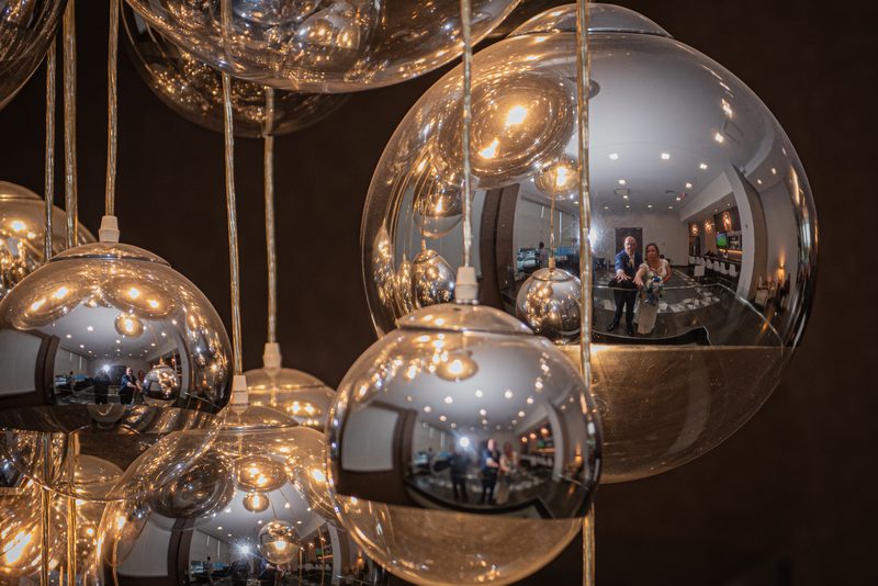 A bride and groom pose within metallic orbs reflecting warm golden light from inside, creating an ethereal scene.