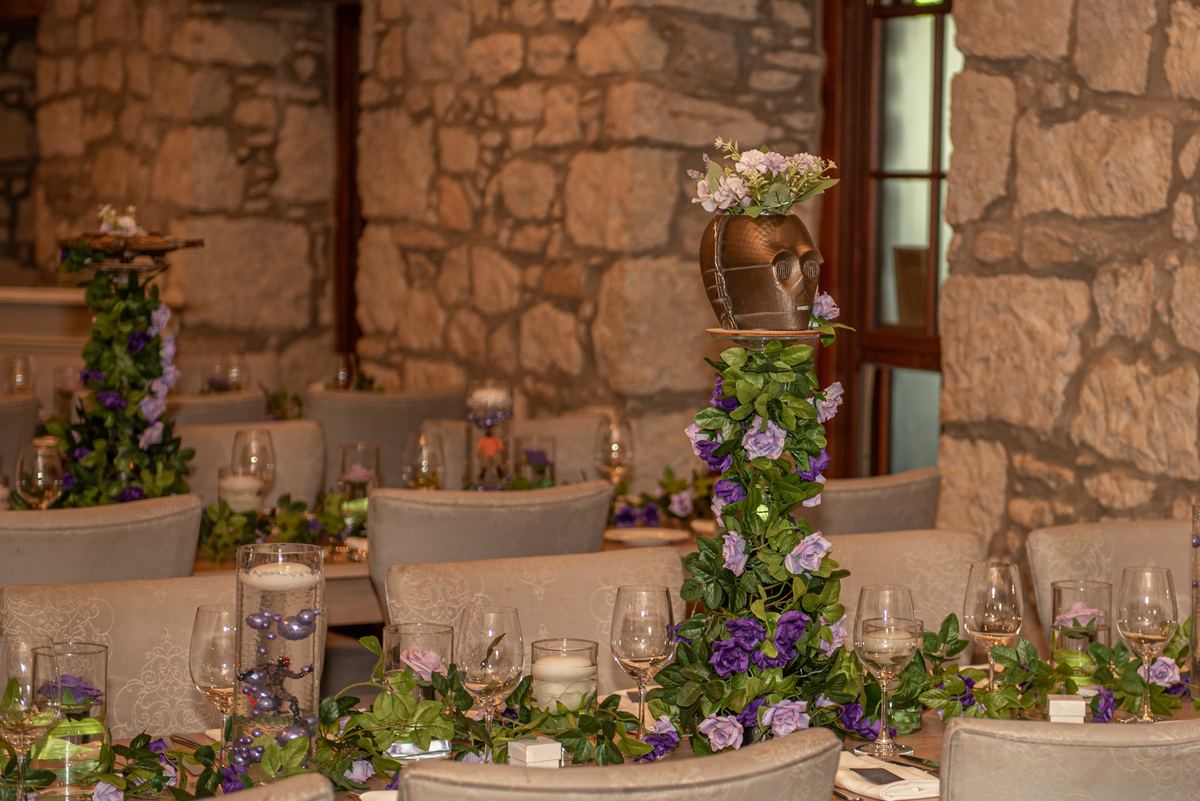A rustic dining table set with greenery and purple flowers, candles, and wine glasses in an intimate celebration setting.