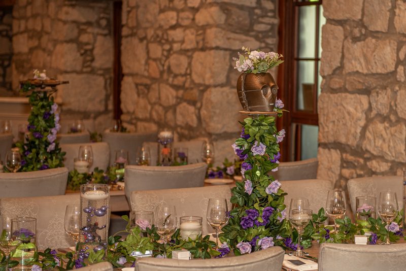 A rustic dining table set with greenery and purple flowers, candles, and wine glasses in an intimate celebration setting.