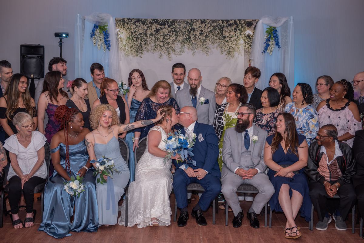 Jennifer and Joe share a tender kiss at their wedding, surrounded by seated guests in festive attire.