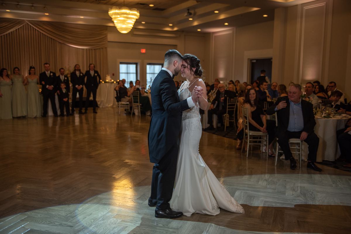 A bride and groom dance intimately under a spotlight, guests watching from the edges of the grand ballroom.