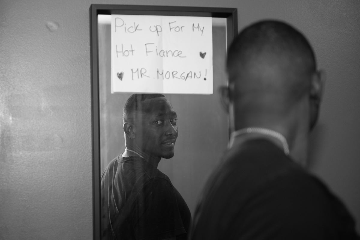 A man stands by a mirror with a playful note from his fiancée visible, reflecting an amused expression.