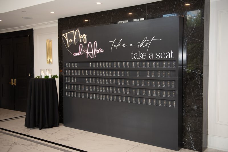 A black marble wall with a shot wall installation and seating area, illuminated by ambient lighting.