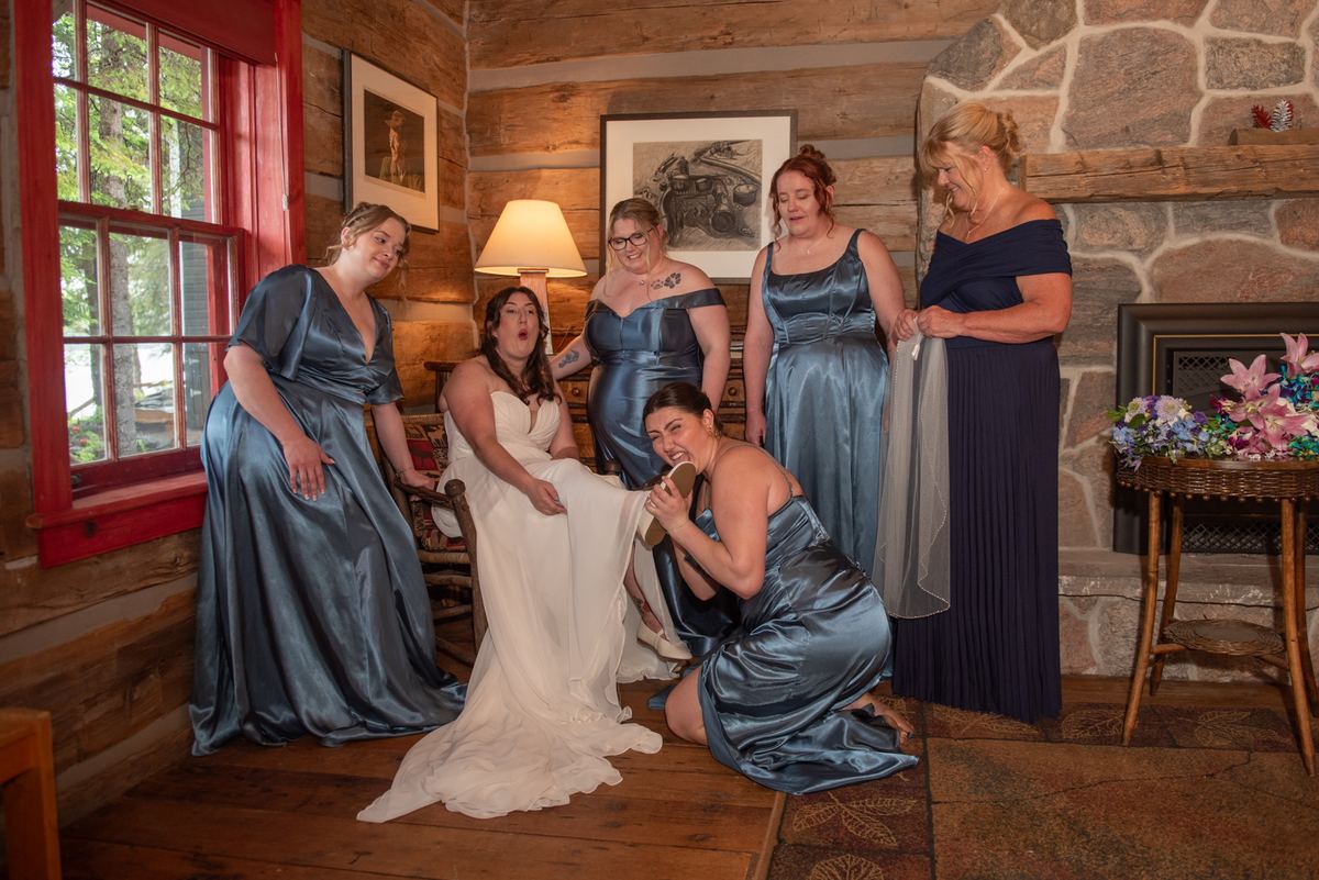 A bride in a white gown is seated among her laughing bridesmaids in blue satin gowns, illuminated by warm cabin light.
