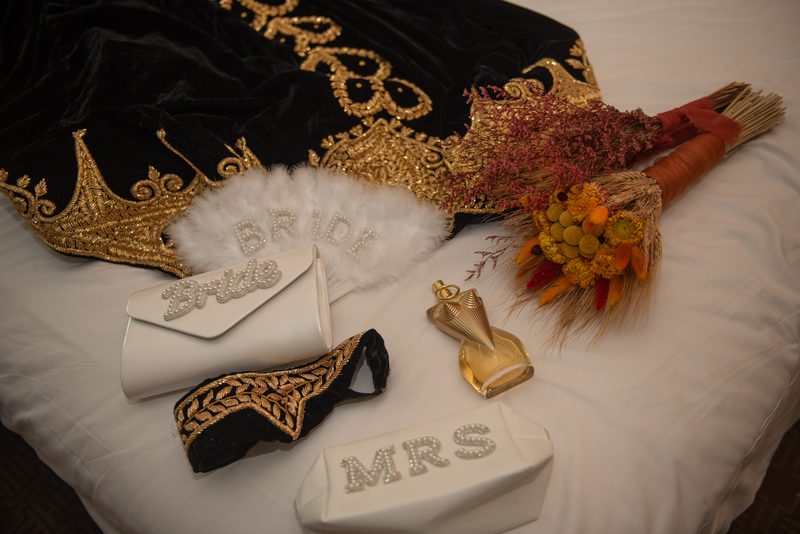 Bridal accessories including a robe, fan, clutch, headband, bouquet, and perfume bottle arranged on a bedspread.