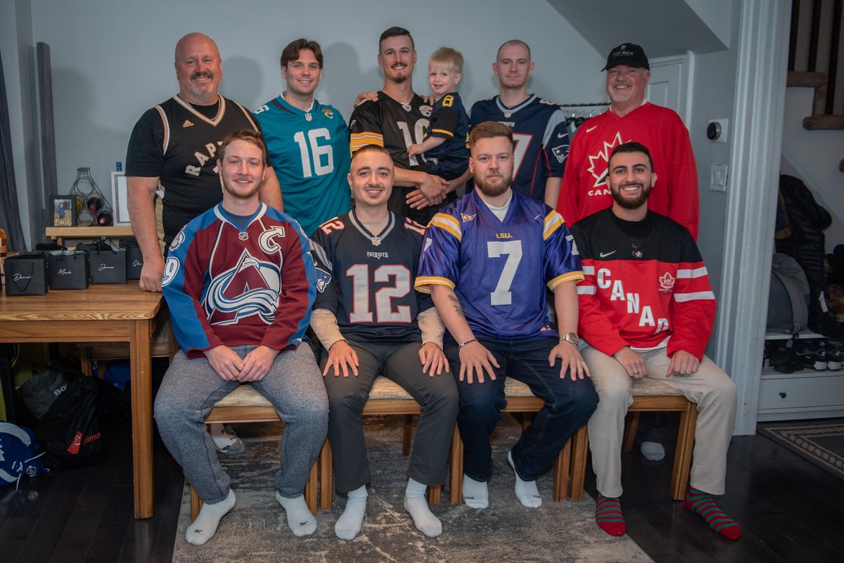Nine men and a young boy in sports jerseys pose cheerfully indoors, under warm lighting, suggesting a fan gathering.