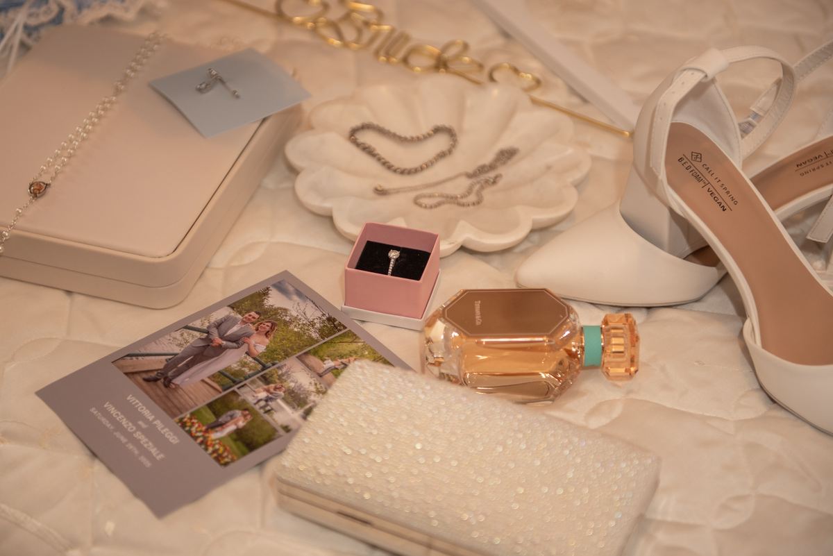 Wedding accessories including a clutch, perfume bottle, heels, and photo card are arranged on a textured surface.
