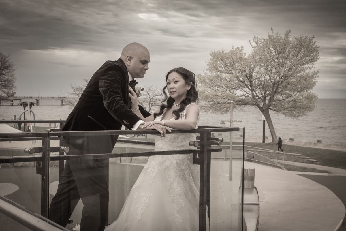 Myrelle and Randy stand closely on a waterfront balcony, the groom leaning towards the bride as they gaze at each other.