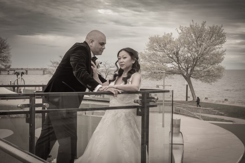 Myrelle and Randy stand closely on a waterfront balcony, the groom leaning towards the bride as they gaze at each other.