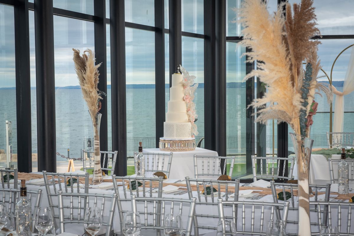 A serene indoor wedding reception with sea view through windows, lit by soft daylight and featuring a white cake.