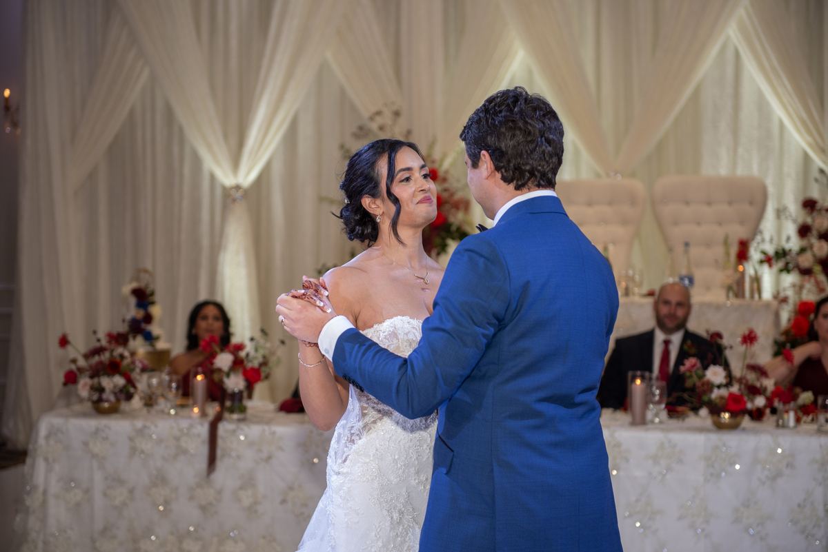 A bride and groom dance intimately under draped white fabric, surrounded by elegantly decorated tables.