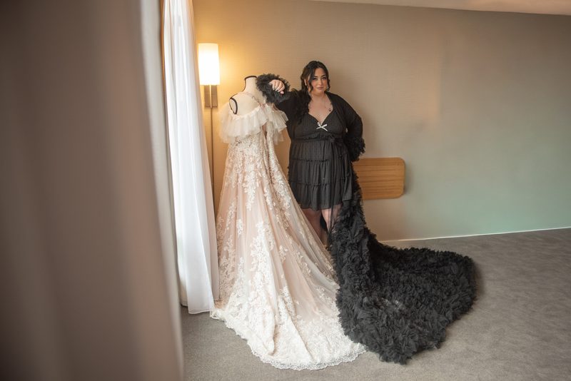 A woman stands beside a mannequin displaying an elaborate lace wedding gown, gently touching the fabric.
