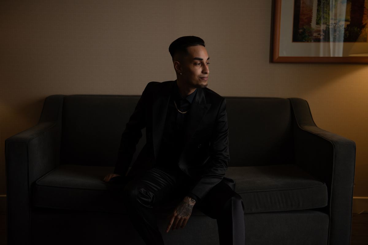 A man in a black suit sits pensively on a sofa, his profile illuminated by soft light from the right.
