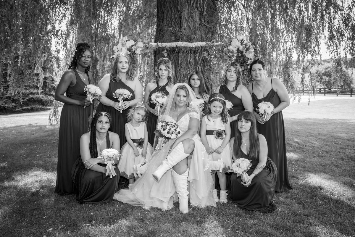 Stephanie and her bridal party pose together under a willow tree, with the bride seated at the center.